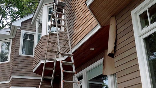 Oiling cedar house using a 40 foot ladder.